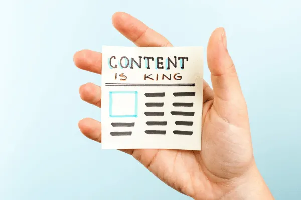 A hand holding a sticky note with the phrase "Content is King" written alongside a simple graphic of a webpage layout.