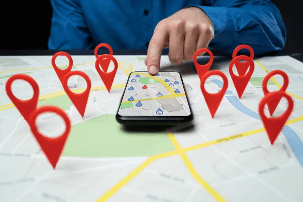 A hand pointing to a smartphone displaying a map with multiple location pins, representing local SEO and business location targeting.
